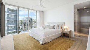 A modern hotel room with a large bed, a nightstand, a ceiling fan, and a view of the city through large windows.