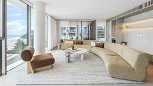 A modern living room with a large sectional sofa, a round coffee table, and a view of the ocean through large windows.