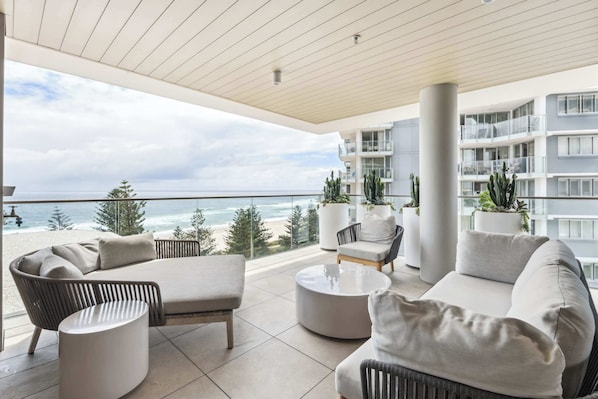 A modern balcony with a view of the ocean, furnished with a sofa, chairs, and a coffee table.