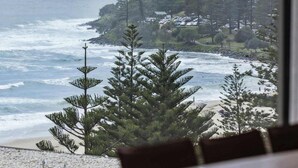 A view from a window overlooking a beach with waves, trees, and buildings in the background.