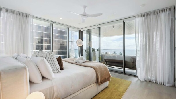 A modern bedroom with a large bed, a view of the balcony, and a ceiling fan.