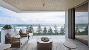 A balcony with a view of the ocean, furnished with wicker furniture and a round table.