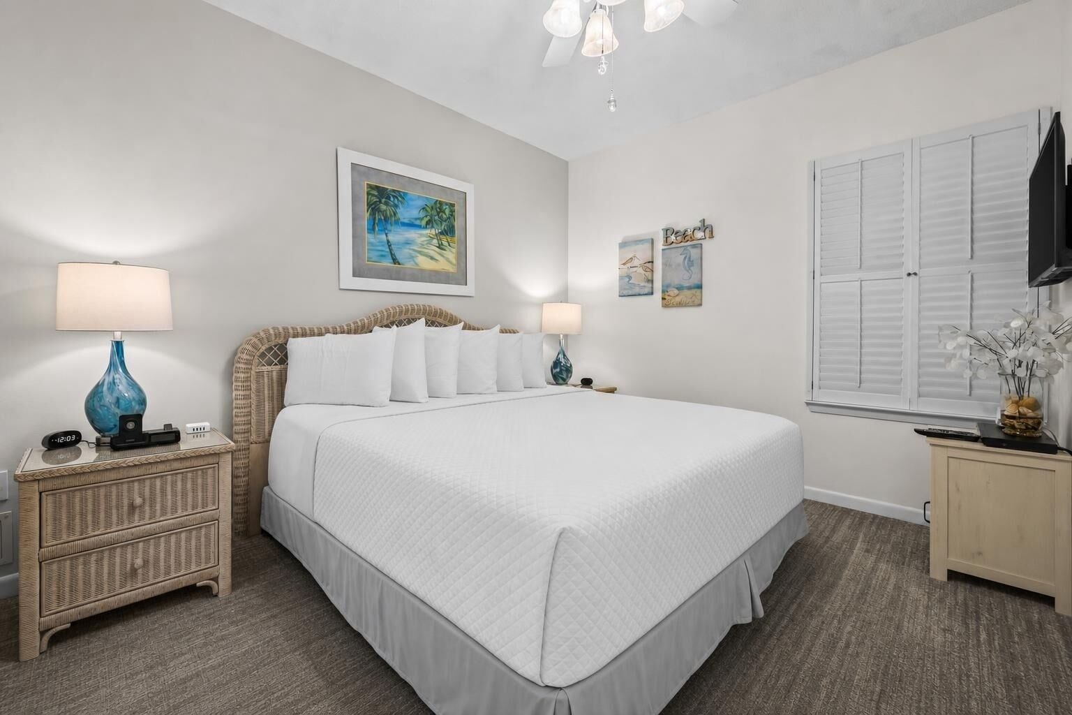A bedroom with a large bed, two bedside tables with lamps, a wall-mounted painting, and a window with shutters.
