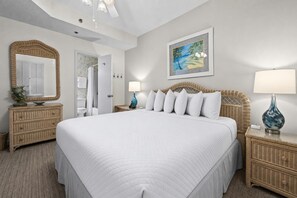 A bedroom with a large bed, a mirror, a painting, and a nightstand with a lamp. - Phoenix East 1205 1 Bedroom Condo (Orange Beach)