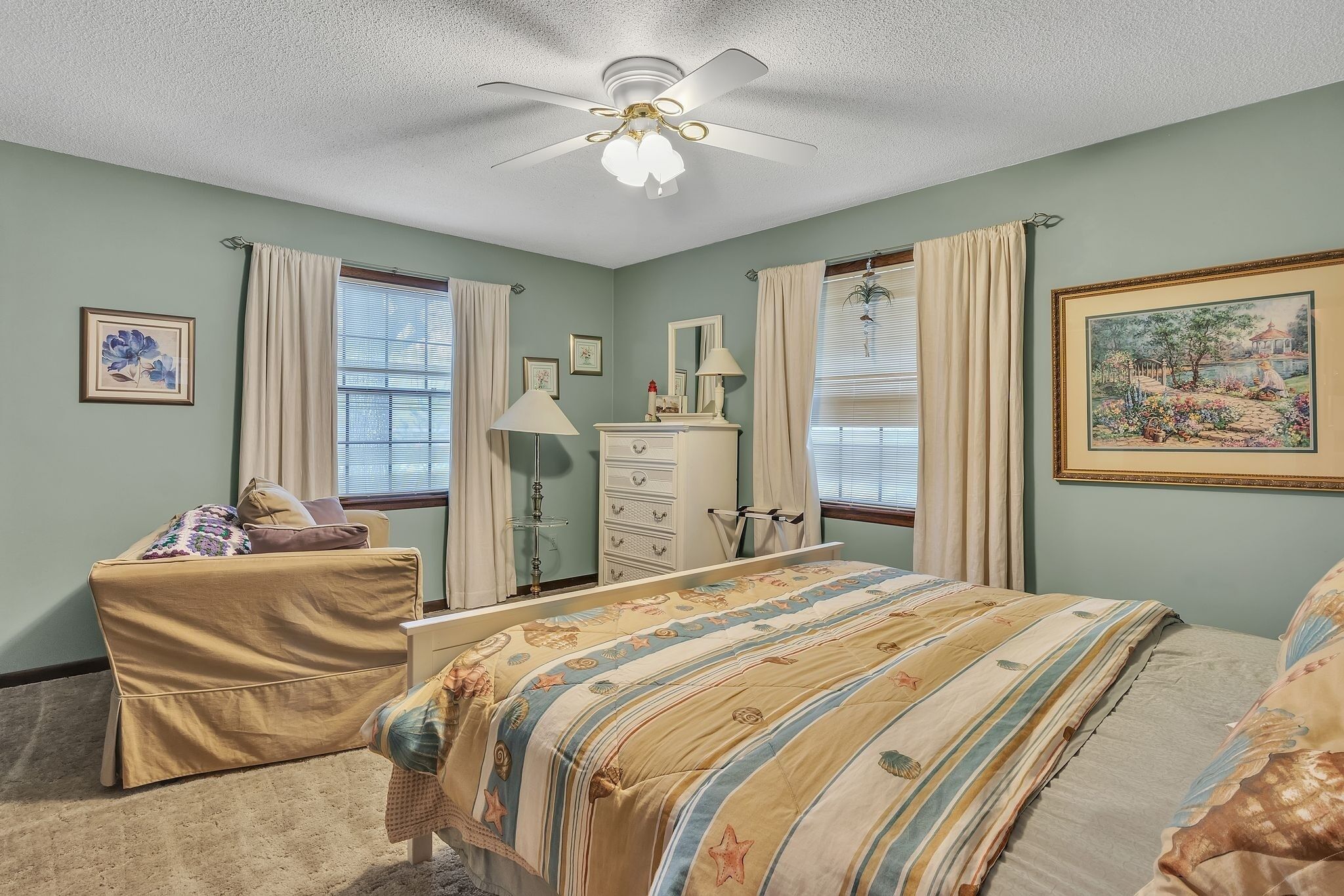 A bedroom with a bed, a dresser, a vanity, a chair, and a ceiling fan.