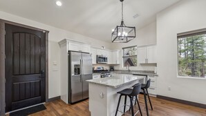 A modern kitchen with white cabinets, stainless steel appliances, a granite countertop, and a large window offering a view of trees.