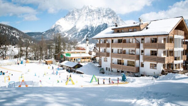 A multi-story building with a snow-covered roof, surrounded by a ski resort with visible ski slopes and a mountain in the background. - Amazing Apartment in Tyrol With Sauna (Lermoos)