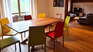 A modern living room with a wooden dining table, colorful chairs, a television, and a large window with curtains. - Wonderful Apartment Close to the ski Slope (Bad Kleinkirchheim)