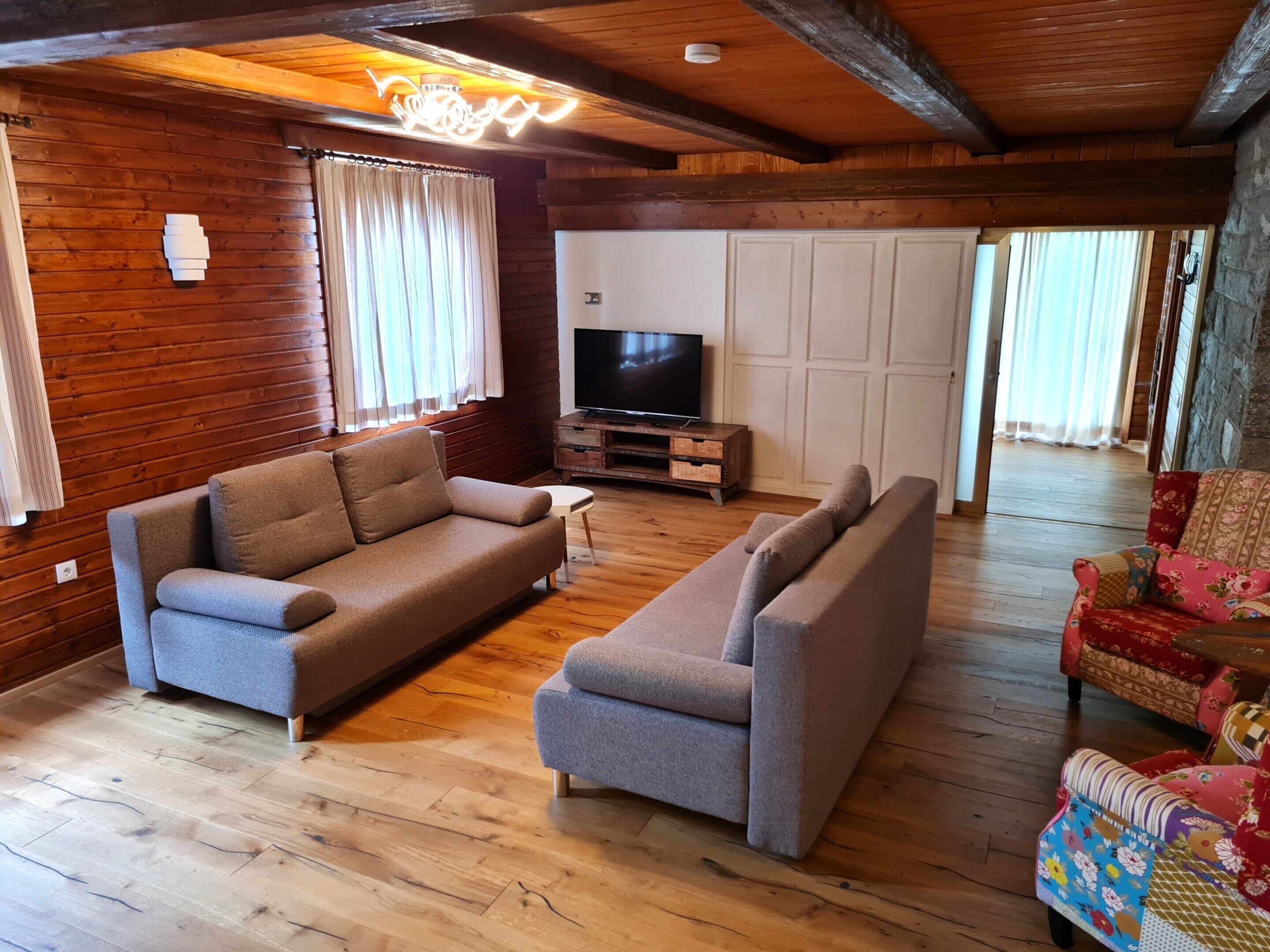 Un salón acogedor con suelo de madera, dos sofás, un televisor sobre un mueble de madera y una pared de piedra.