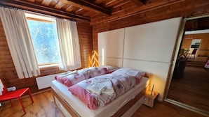 A wooden cabin bedroom with a bed, a red chair, a window with curtains, and a view of the outdoors. - Wonderful Apartment Close to the ski Slope (Bad Kleinkirchheim)