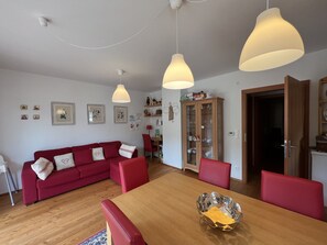 A living room with a red sofa, wooden dining table, and pendant lights.