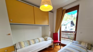 A room with two beds, a red chair, a hanging lamp, and a view of a wooden deck outside. - Central Vacation Apartment With View (Bad Kleinkirchheim)