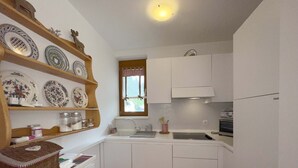A compact kitchen with white cabinets, a sink, and a window with a checkered curtain. - Central Vacation Apartment With View (Bad Kleinkirchheim)