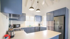 A modern kitchen with blue cabinets, a stainless steel refrigerator, a gas stove, and a large island. - Inch By Inch 3 Bedroom Home by Bluescape (Silver Sands)