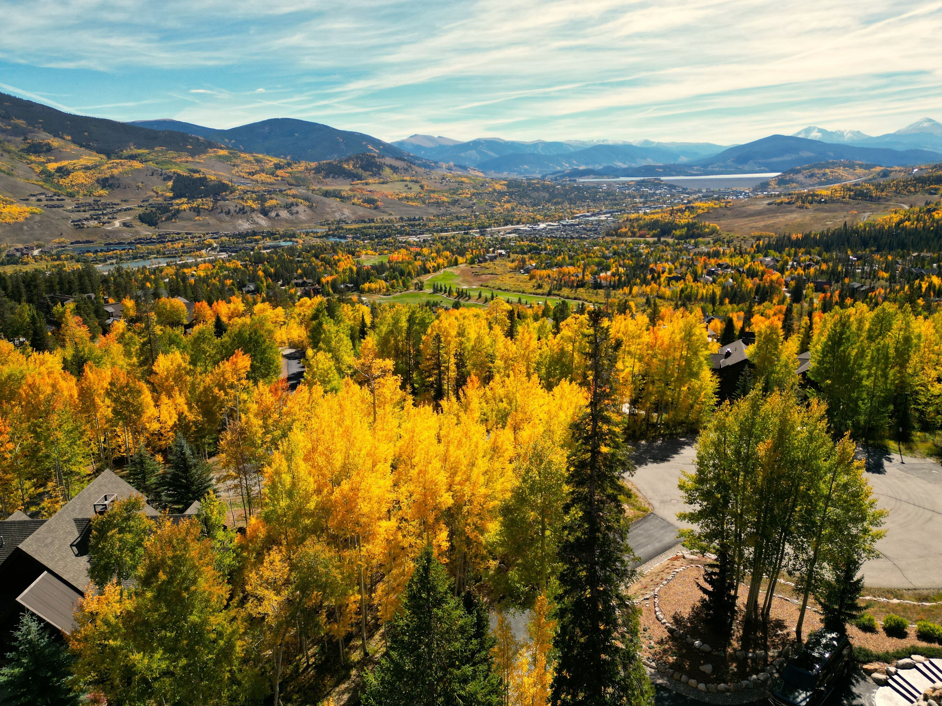 Un quartier résidentiel où les maisons sont entourées d’arbres aux couleurs automnales, avec un petit lac et des montagnes qui se dessinent à l’horizon.