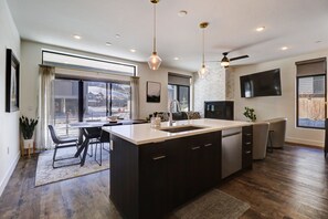 Una cocina moderna con una isla central, iluminación colgante y un ventilador de techo.