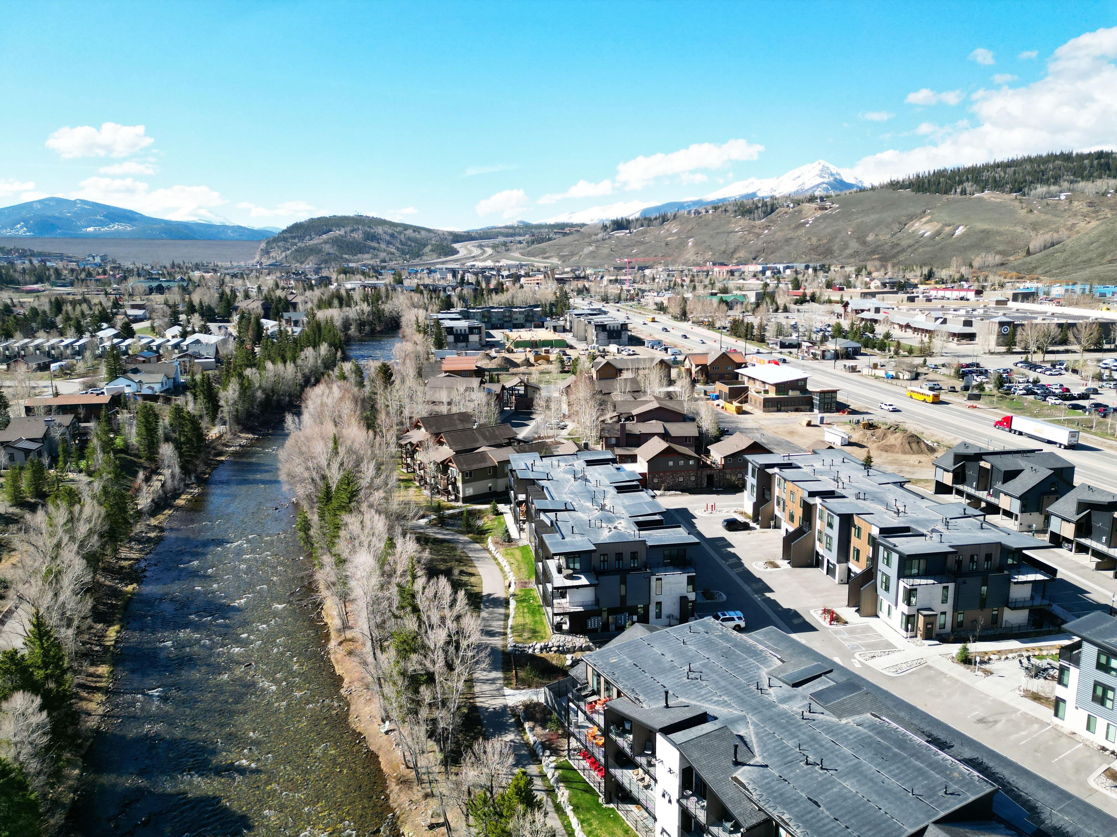 A residential area with houses along a river, a highway, and mountains in the background.