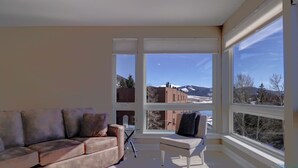 A living room with a beige sofa, a small white table, and a view of mountains through large windows. - Sail Lofts 205 2 Bedroom Condo (Dillon)