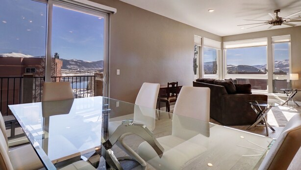 A modern living room with a glass dining table, comfortable seating, and large windows offering mountain views. - Sail Lofts 205 2 Bedroom Condo (Dillon)
