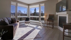 A spacious living room with a large window, a fireplace, and a ceiling fan. - Sail Lofts 205 2 Bedroom Condo (Dillon)