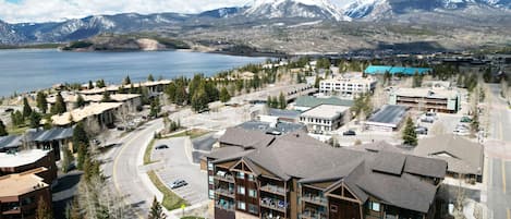 A modern hotel with multiple floors, a parking lot, and a view of a lake and mountains in the background.