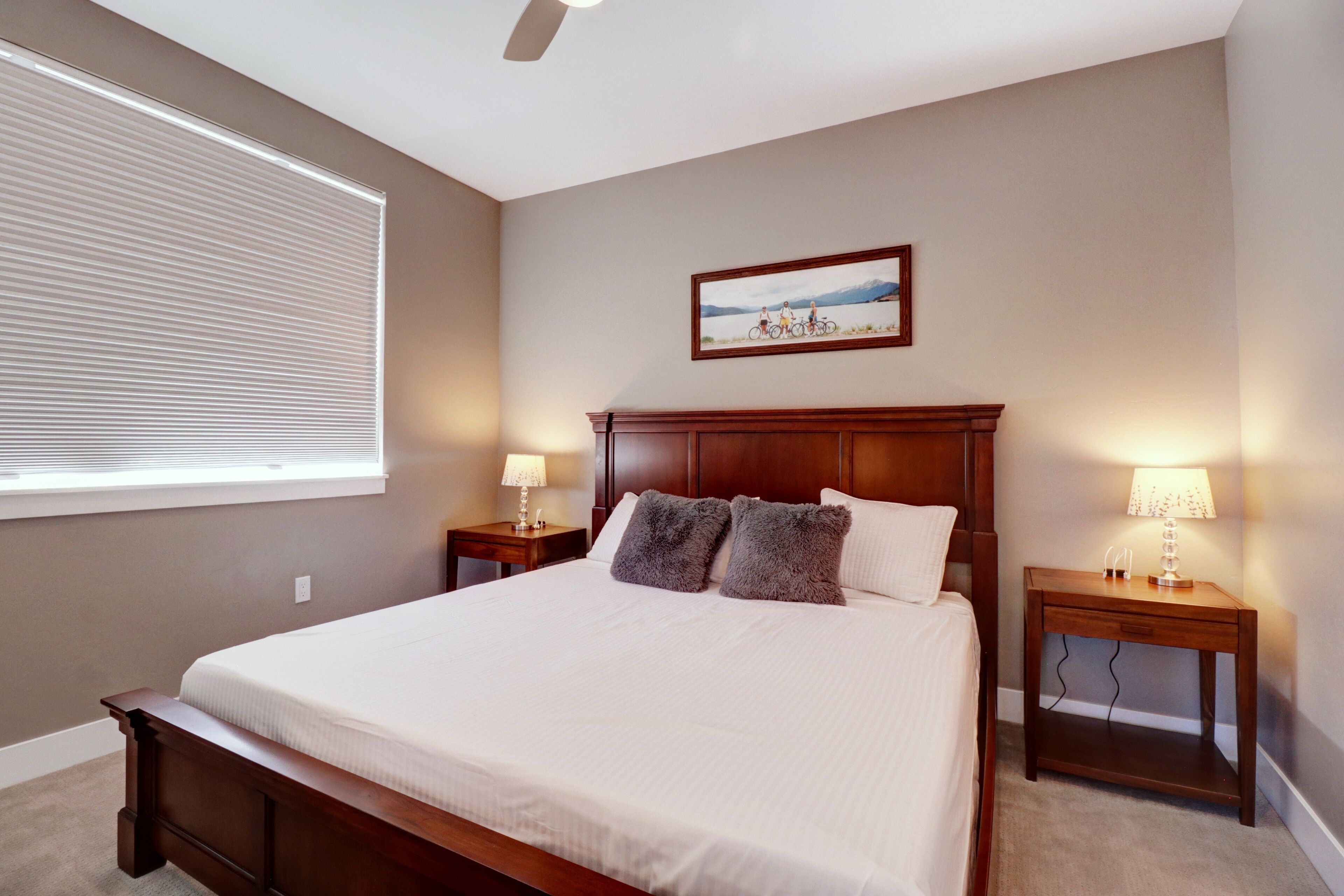 Une chambre à coucher avec un grand lit, deux tables de chevet avec des lampes, un ventilateur de plafond et un tableau encadré au mur.