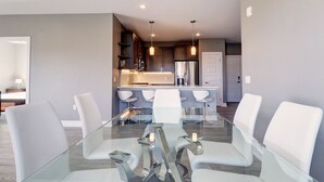 A modern kitchen with stainless steel appliances, a glass dining table with white chairs, and recessed ceiling lighting. - Sail Lofts 205 2 Bedroom Condo (Dillon)
