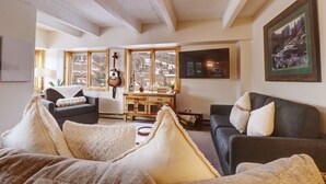 Un salón acogedor con chimenea, una guitarra y un ventanal con vistas a un paisaje nevado.