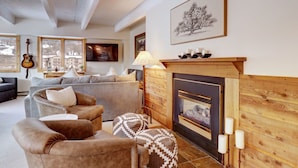 Una sala de estar acogedora con chimenea, un sofá, sillones y un otoman estampado.