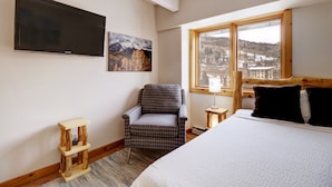 Un dormitorio con cama, una silla, un televisor, un ventanal y una lámpara.