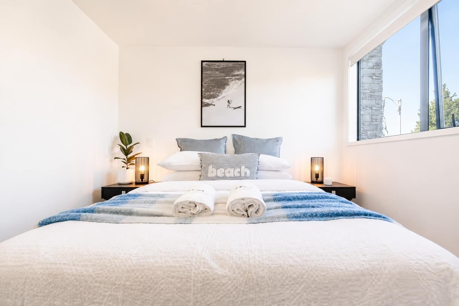 A neatly made bed with a blue and white striped blanket, two bedside lamps, and a framed picture on the wall.