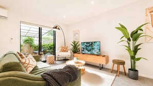 Ein modernes Wohnzimmer mit einer Couch, einem Couchtisch, einem Fernseher und einer großen Pflanze.