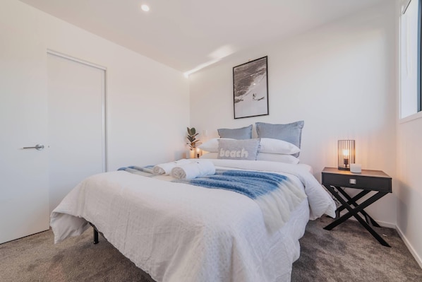 A neatly arranged bedroom with a bed, pillows, a bedside table with a lamp, and a framed picture on the wall.