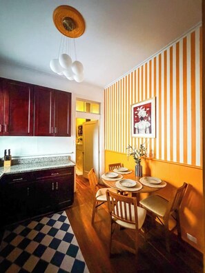 A kitchen with dark cabinets, a checkered floor, and a dining area with striped wallpaper and a table set for four.