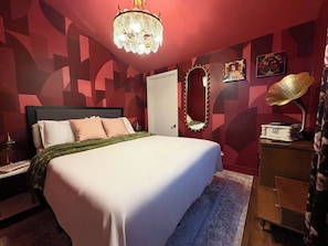 A bedroom with a bed, a nightstand, a dresser, a mirror, and a chandelier. - "La Lune Noire NOLA" (New Orleans)
