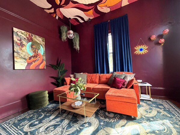 A room with a vibrant orange sofa, a glass coffee table, and a patterned rug.