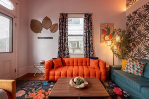 A living room with a sofa, a coffee table, and a window with curtains. - Delightful Design & Cowboy Pool by French Quarter (New Orleans)