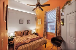 A bedroom with a bed, a chair, a ceiling fan, a window with curtains, and a door. - Delightful Design & Cowboy Pool by French Quarter (New Orleans)