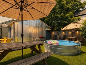 Un patio trasero con piscina, mesa de madera, sillas y un paraguas grande.