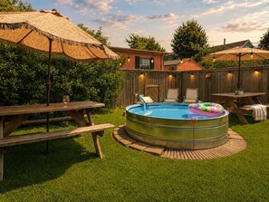 Un jardin avec une piscine ronde, des tables de pique-nique et un parasol en chaume.