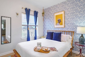 Habitación de hotel con cama, mesita de noche, lámpara, bandeja de desayuno y ventana con cortinas.