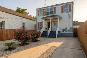 A two-story house with a front porch, a staircase, and a small garden with pink flowers. - Spacious Retreat by FQ | Mini-Pool | EV Parking (New Orleans)