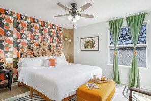 Ein Schlafzimmer mit einem Bett, einem Deckenventilator, einem Fenster mit Vorhängen und einer Wand mit einem geometrischen Muster.
