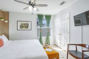 A bedroom with a bed, a chair, a ceiling fan, a window with curtains, and a television on the wall. - Spacious Retreat by FQ | Mini-Pool | EV Parking (New Orleans)