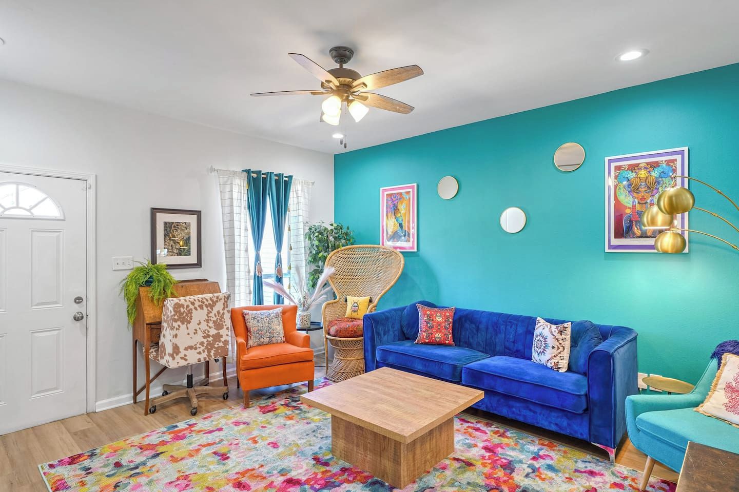 Una sala de estar con un sofá azul, un sillón naranja y un ventilador de techo.