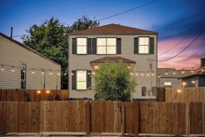 A two-story house with a wooden fence, string lights, and a tree in the yard. - Spacious Retreat by FQ | Mini-Pool | EV Parking (New Orleans)