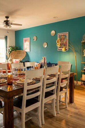 Un comedor con una mesa de madera y sillas blancas, paredes color aguamarina y un ventilador de techo.