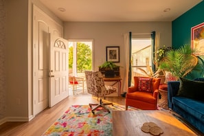 A living room with a wooden floor, a colorful rug, a blue sofa, a red armchair, a patterned armchair, and a dining area with a table and chairs. - Spacious Retreat by FQ | Mini-Pool | EV Parking (New Orleans)