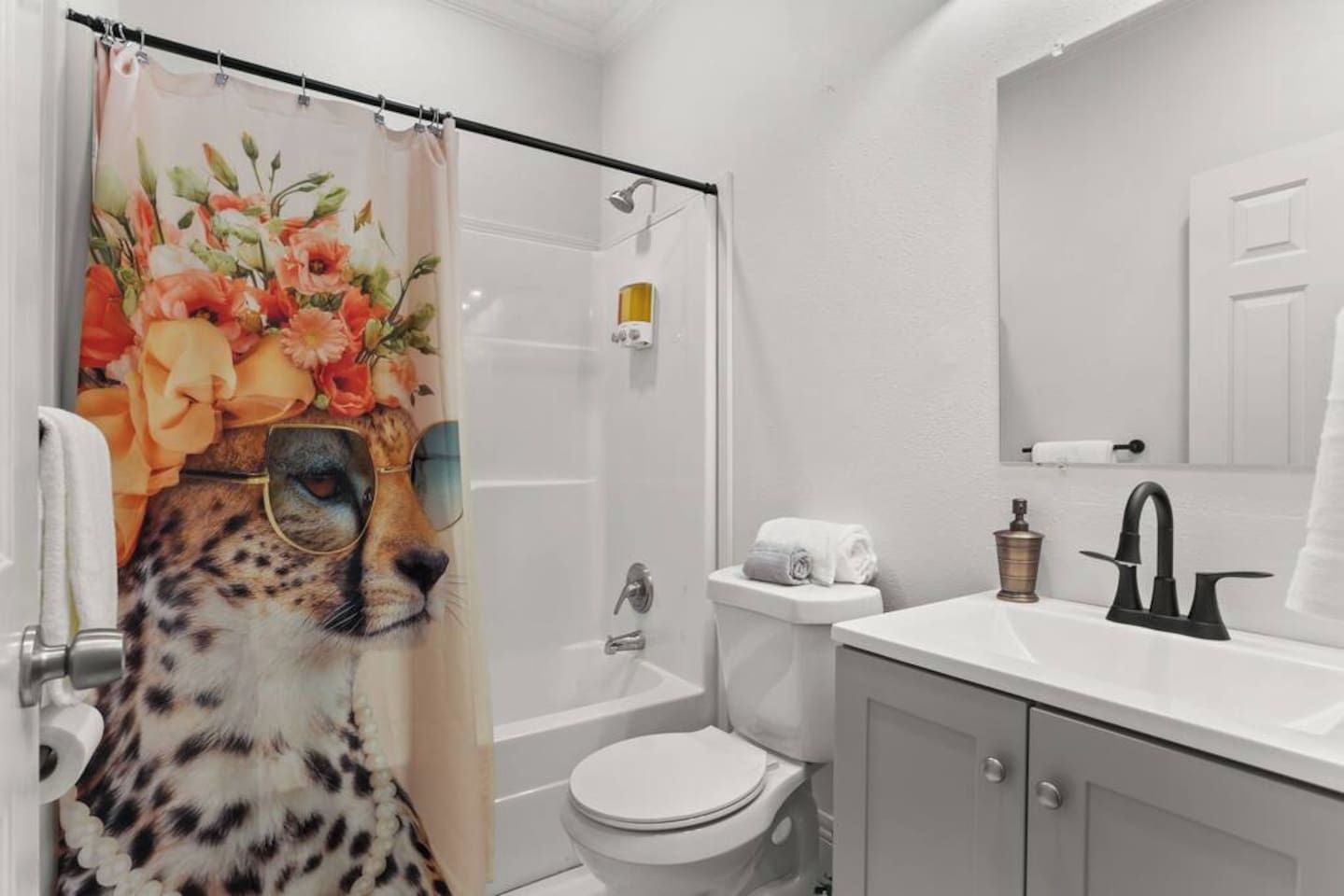 A bathroom with a shower curtain, toilet, sink, and mirror.