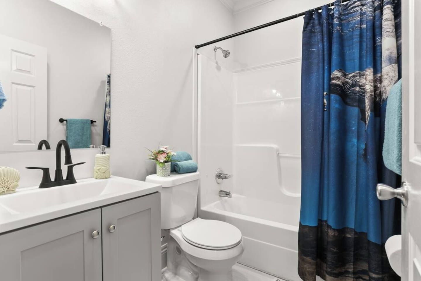A bathroom with a white sink, a toilet, a shower, and a blue shower curtain.